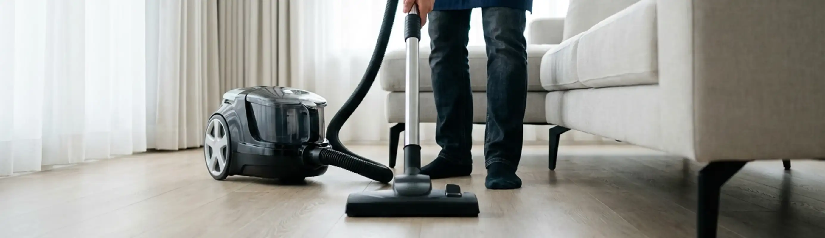 Professional house cleaner vacuuming a living room floor with a canister vacuum cleaner, Wichita, KS.